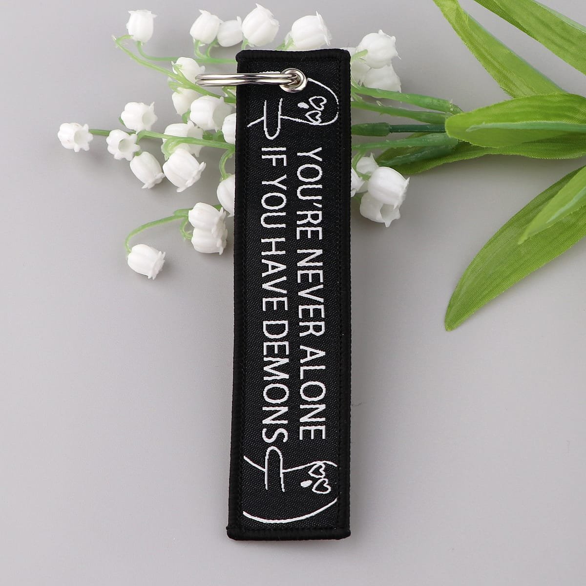 Mustast materjalist mootorratta võtmehoidja, mille servale on tikitud "You're never alone if you have demons".