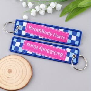 Back&Body Hurts võtmehoidja on mustast materjalist aksessuaar, millele on tikitud valgete, punaste ja roosade triipudega kiri.