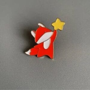An orange leaf with a white chest and tail tip holds a yellow star enamel brooch fairy tale motifs