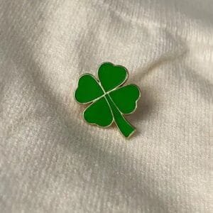 A rich green four-leaf clover with a golden outline pinned to a white sweater enamel pin symbol of good luck