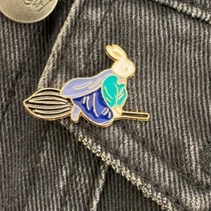 A white rabbit with a blue cloak flying on a witch's broomstick enamel pin fantasy fairy tales