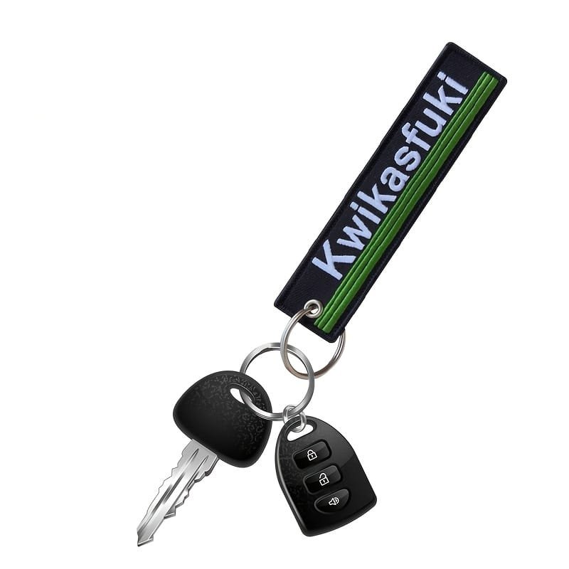 Juodas tekstilinis raktų pakabukas su užrašu „Kwikasfuki“ ir žaliomis juostelėmis prie automobilio raktų